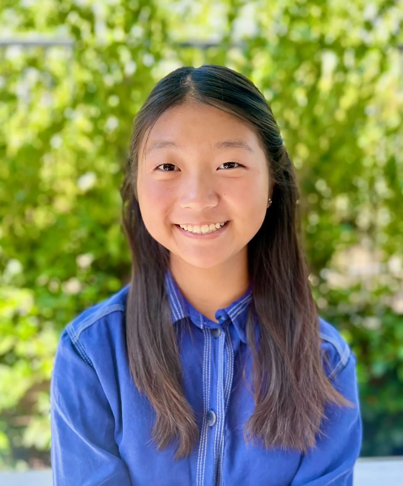 Alexia Kim in a blue button-up shirt against a background of blurred green foliage