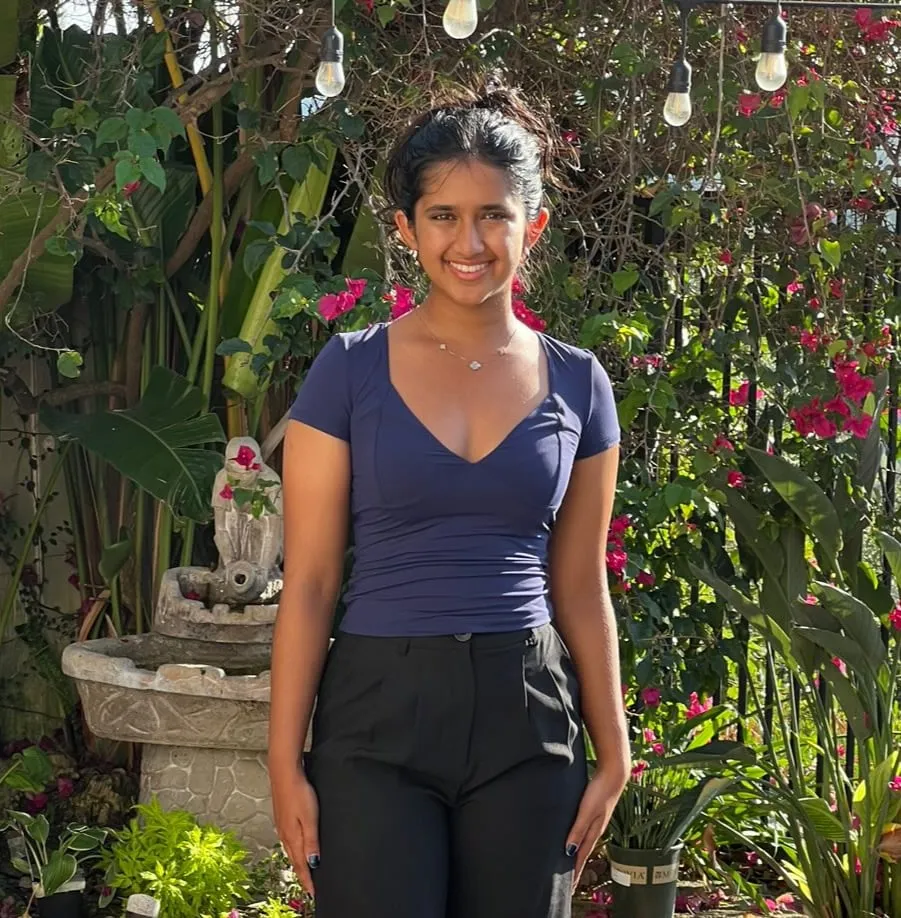 Carina Leo in a garden with bougainvillea and string lights, wearing a navy short-sleeve top and black trousers