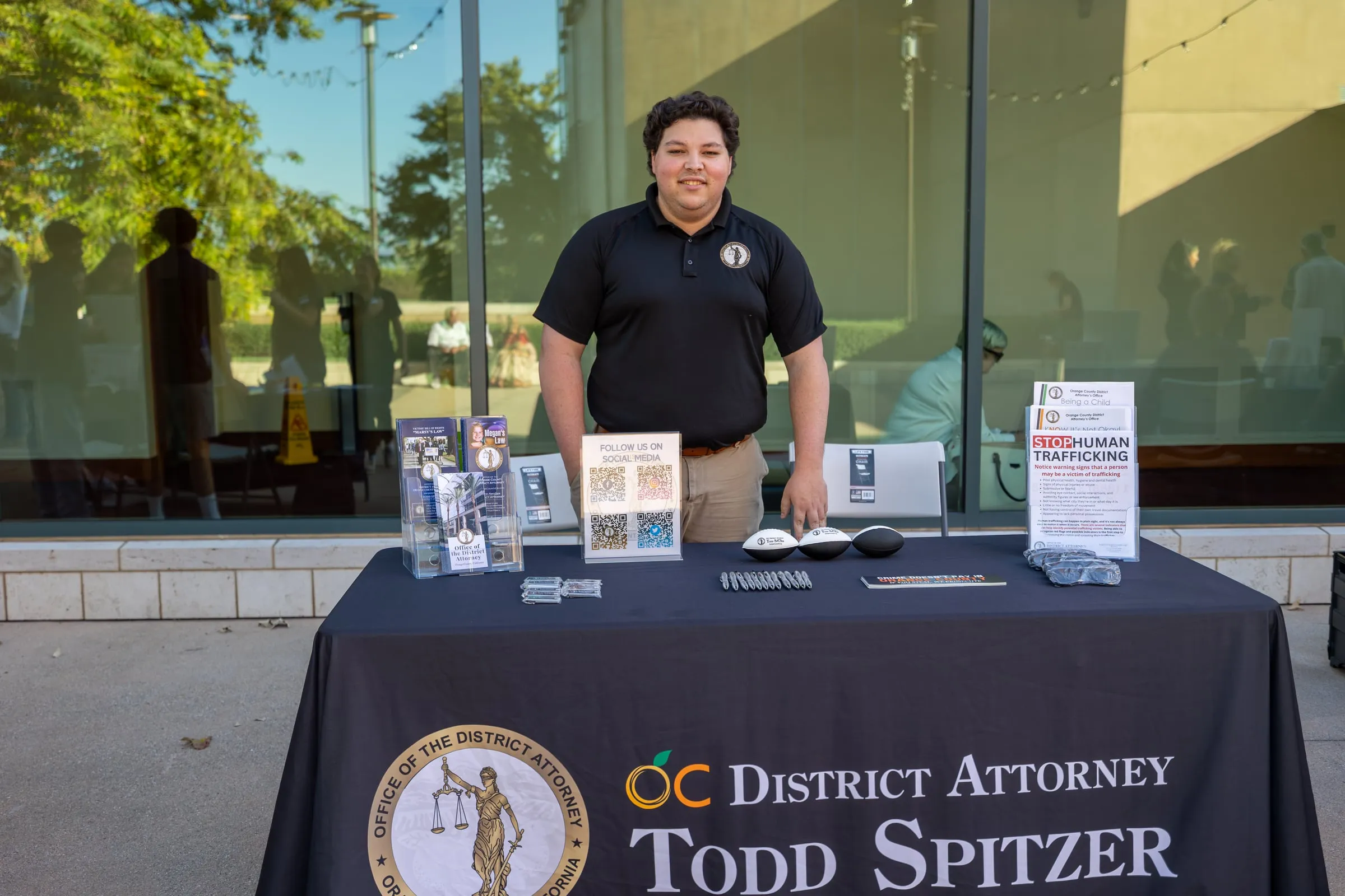 A volunteer stands behind the Orange County District Attorney Todd Spitzer resource table, laid out with brochures, a "Stop Human Trafficking" sign and giveaway items