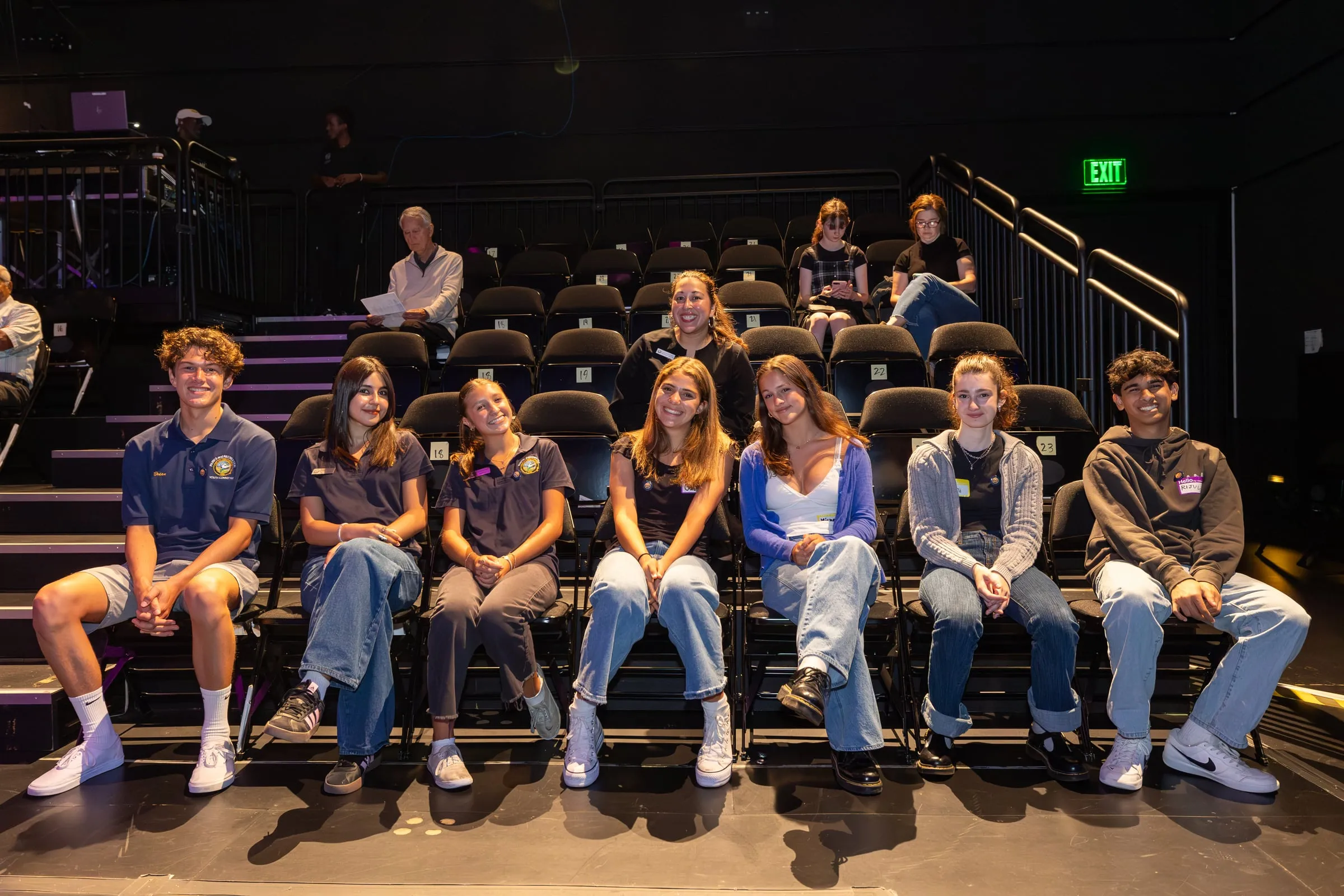 Eight young volunteers sit along the front row of the theatre's tiered seating, turning to face the camera
